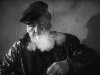 Movie still from “The Docks of New York” (1928), directed by Josef von Sternberg – An older man smoking a cigarette in a black and white photo; Close Up shot, High angle