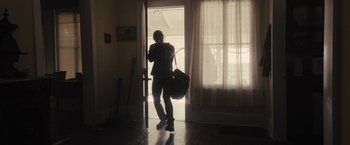 Movie still from “The Domestics” (2018), directed by Mike P. Nelson – A man is holding a bag while standing in front of a door; Wide shot, Low angle