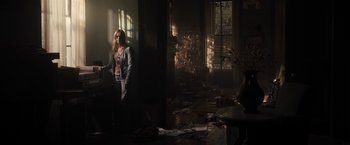 Movie still from “The Domestics” (2018), directed by Mike P. Nelson – A woman standing in a living room in the sunlight; Wide shot, High angle