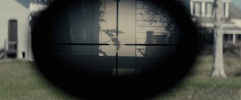 Movie still from “The Domestics” (2018), directed by Mike P. Nelson – A view through a rifle scope of a window; Extreme Close Up shot, Overhead angle