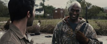 Movie still from “The Domestics” (2018), directed by Mike P. Nelson – A man in a camouflage jacket talking to another man; Close Up shot, Over the shoulder angle