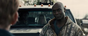 Movie still from “The Domestics” (2018), directed by Mike P. Nelson – A man standing in front of a truck with two women in the background; Close Up shot, Over the shoulder angle