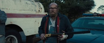 Movie still from “The Domestics” (2018), directed by Mike P. Nelson – A man with a beard holding a rifle; Medium shot, Low angle