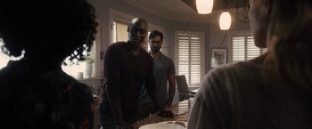 Movie still from “The Domestics” (2018), directed by Mike P. Nelson – Two men standing at a counter in front of a cake; Medium shot, Over the shoulder angle