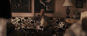 Movie still from “The Domestics” (2018), directed by Mike P. Nelson – A man sitting on top of a couch holding a cell phone; Wide shot, Low angle