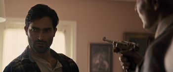 Movie still from “The Domestics” (2018), directed by Mike P. Nelson – A man holding a gun pointed at another man in a living room; Close Up shot, Over the shoulder angle