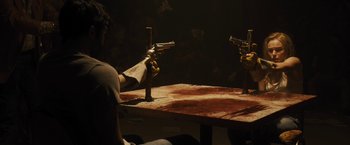 Movie still from “The Domestics” (2018), directed by Mike P. Nelson – A man holding a pair of pistols on top of a table; Medium shot, Over the shoulder angle