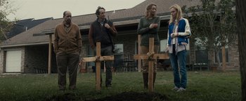 Movie still from “The Domestics” (2018), directed by Mike P. Nelson – A group of people standing next to wooden crosses in the grass; Medium shot, Over the shoulder angle