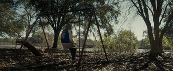 Movie still from “The Domestics” (2018), directed by Mike P. Nelson – A woman sitting on a swing in a park; Wide shot, Over the shoulder angle
