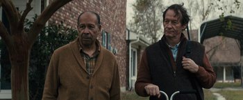 Movie still from “The Domestics” (2018), directed by Mike P. Nelson – Two men standing next to each other in front of a brick building; Medium shot, Over the shoulder angle