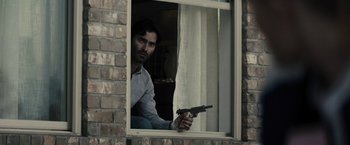 Movie still from “The Domestics” (2018), directed by Mike P. Nelson – A man holding a gun in front of a window; Medium shot, Low angle
