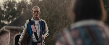 Movie still from “The Domestics” (2018), directed by Mike P. Nelson – A woman standing in front of a tree holding a pole; Medium shot, Over the shoulder angle