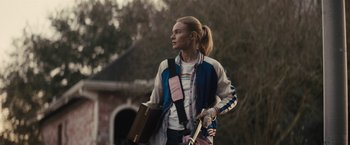Movie still from “The Domestics” (2018), directed by Mike P. Nelson – A woman holding a book and a guitar; Medium shot, Over the shoulder angle