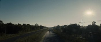 Movie still from “The Domestics” (2018), directed by Mike P. Nelson – A car driving down a road near a forest; Extreme Wide shot, High angle