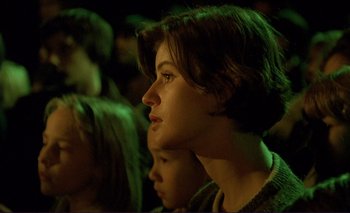 Movie still from “The Double Life of Véronique” (1991), directed by Krzysztof Kieslowski – A person sitting in a crowd of people; Close Up shot, Over the shoulder angle