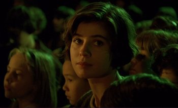 Movie still from “The Double Life of Véronique” (1991), directed by Krzysztof Kieslowski – A woman with short brown hair sitting in front of a group of people; Close Up shot, High angle