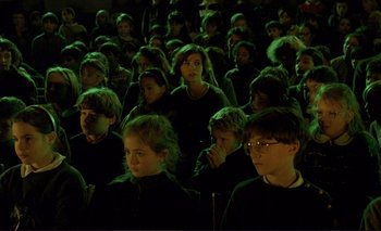 Movie still from “The Double Life of Véronique” (1991), directed by Krzysztof Kieslowski – A group of people sitting in a dark room; Medium shot, High angle