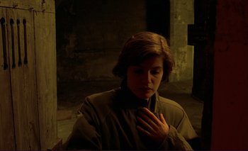 Movie still from “The Double Life of Véronique” (1991), directed by Krzysztof Kieslowski – A woman is sitting in a dark room with her hand on her chest; Medium shot, High angle