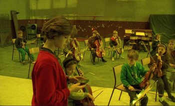 Movie still from “The Double Life of Véronique” (1991), directed by Krzysztof Kieslowski – A group of people sitting in a room with musical instruments; Wide shot, High angle