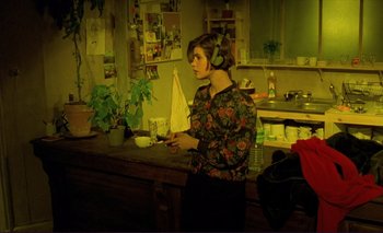 Movie still from “The Double Life of Véronique” (1991), directed by Krzysztof Kieslowski – A woman standing in a kitchen holding a cell phone; Medium shot, High angle