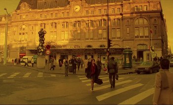 Movie still from “The Double Life of Véronique” (1991), directed by Krzysztof Kieslowski – A group of people walking across a crosswalk in front of a building; Extreme Wide shot, High angle