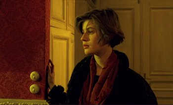 Movie still from “The Double Life of Véronique” (1991), directed by Krzysztof Kieslowski – A woman with short brown hair wearing a black coat and a red scarf; Medium shot, Over the shoulder angle
