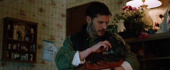 Movie still from “The Drop” (2014), directed by Michaël R. Roskam – A man in a green jacket is holding something in his hand; Close Up shot, High angle