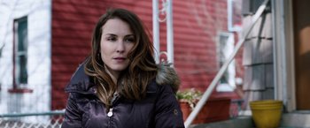 Movie still from “The Drop” (2014), directed by Michaël R. Roskam – A woman in a black jacket standing in front of a red building; Close Up shot, Over the shoulder angle