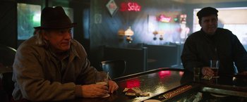 Movie still from “The Drop” (2014), directed by Michaël R. Roskam – A man sitting at a bar with a glass of beer; Medium shot, Over the shoulder angle