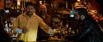 Movie still from “The Drop” (2014), directed by Michaël R. Roskam – Two men standing at a bar with a bottle of alcohol; Medium shot, Over the shoulder angle