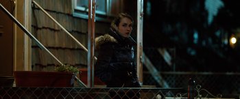 Movie still from “The Drop” (2014), directed by Michaël R. Roskam – A woman wearing a black jacket standing next to a fence; Medium shot, Over the shoulder angle