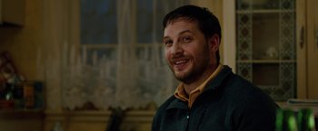 Movie still from “The Drop” (2014), directed by Michaël R. Roskam – A man smiling for the camera in front of a window; Close Up shot, Over the shoulder angle