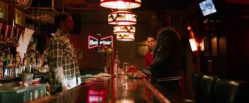 Movie still from “The Drop” (2014), directed by Michaël R. Roskam – A group of people sitting at a bar with drinks; Medium shot, Over the shoulder angle