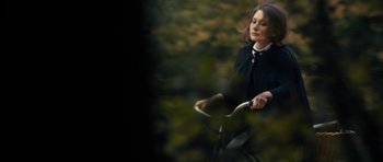 Movie still from “The Duke of Burgundy” (2014), directed by Peter Strickland – A woman riding a bike through a forest; Medium shot, Over the shoulder angle
