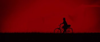 Movie still from “The Duke of Burgundy” (2014), directed by Peter Strickland – A person riding a bike on a field near trees; Extreme Wide shot, Overhead angle