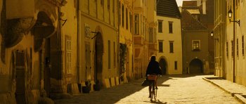 Movie still from “The Duke of Burgundy” (2014), directed by Peter Strickland – A person riding a bike down a street; Extreme Wide shot, Low angle