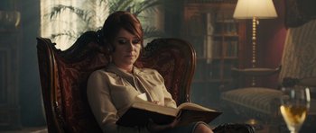 Movie still from “The Duke of Burgundy” (2014), directed by Peter Strickland – A woman sitting in a chair reading a book; Medium shot, Over the shoulder angle