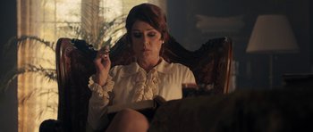 Movie still from “The Duke of Burgundy” (2014), directed by Peter Strickland – A woman sitting in a chair reading a book; Medium shot, Over the shoulder angle