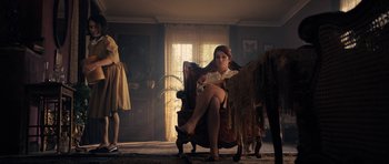 Movie still from “The Duke of Burgundy” (2014), directed by Peter Strickland – A woman sitting in a chair in a living room next to a horse; Wide shot, Low angle