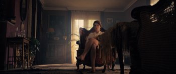 Movie still from “The Duke of Burgundy” (2014), directed by Peter Strickland – A woman sitting in a chair in a living room; Wide shot, Low angle