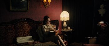 Movie still from “The Duke of Burgundy” (2014), directed by Peter Strickland – A woman sitting in a chair holding a glass of wine; Medium shot, Low angle