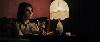 Movie still from “The Duke of Burgundy” (2014), directed by Peter Strickland – A woman sitting in front of a table holding a glass of wine; Medium shot, Over the shoulder angle