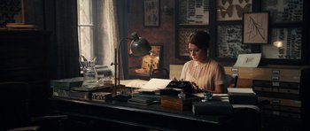 Movie still from “The Duke of Burgundy” (2014), directed by Peter Strickland – A woman sitting at a desk looking at papers on top of a desk; Medium shot, High angle