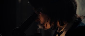 Movie still from “The Duke of Burgundy” (2014), directed by Peter Strickland – A woman looking through a microscope in the dark; Extreme Close Up shot, Low angle