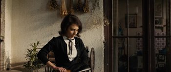 Movie still from “The Duke of Burgundy” (2014), directed by Peter Strickland – A woman sitting in a chair looking down at a piece of paper; Medium shot, Over the shoulder angle