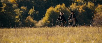 Movie still from “The Duke of Burgundy” (2014), directed by Peter Strickland – A man and a woman riding bikes through a field; Extreme Wide shot, High angle