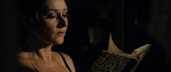 Movie still from “The Duke of Burgundy” (2014), directed by Peter Strickland – A person holding a book in a dark room; Close Up shot, Over the shoulder angle