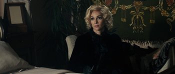 Movie still from “The Duke of Burgundy” (2014), directed by Peter Strickland – A woman with blonde hair sitting at a table; Medium shot, Over the shoulder angle