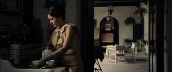 Movie still from “The Duke of Burgundy” (2014), directed by Peter Strickland – A woman standing in front of a table holding a cup; Medium shot, Over the shoulder angle