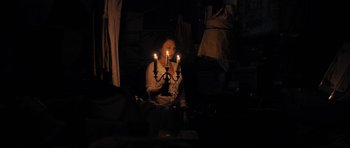 Movie still from “The Duke of Burgundy” (2014), directed by Peter Strickland – A person sitting in a chair holding a lit candle; Medium shot, Over the shoulder angle